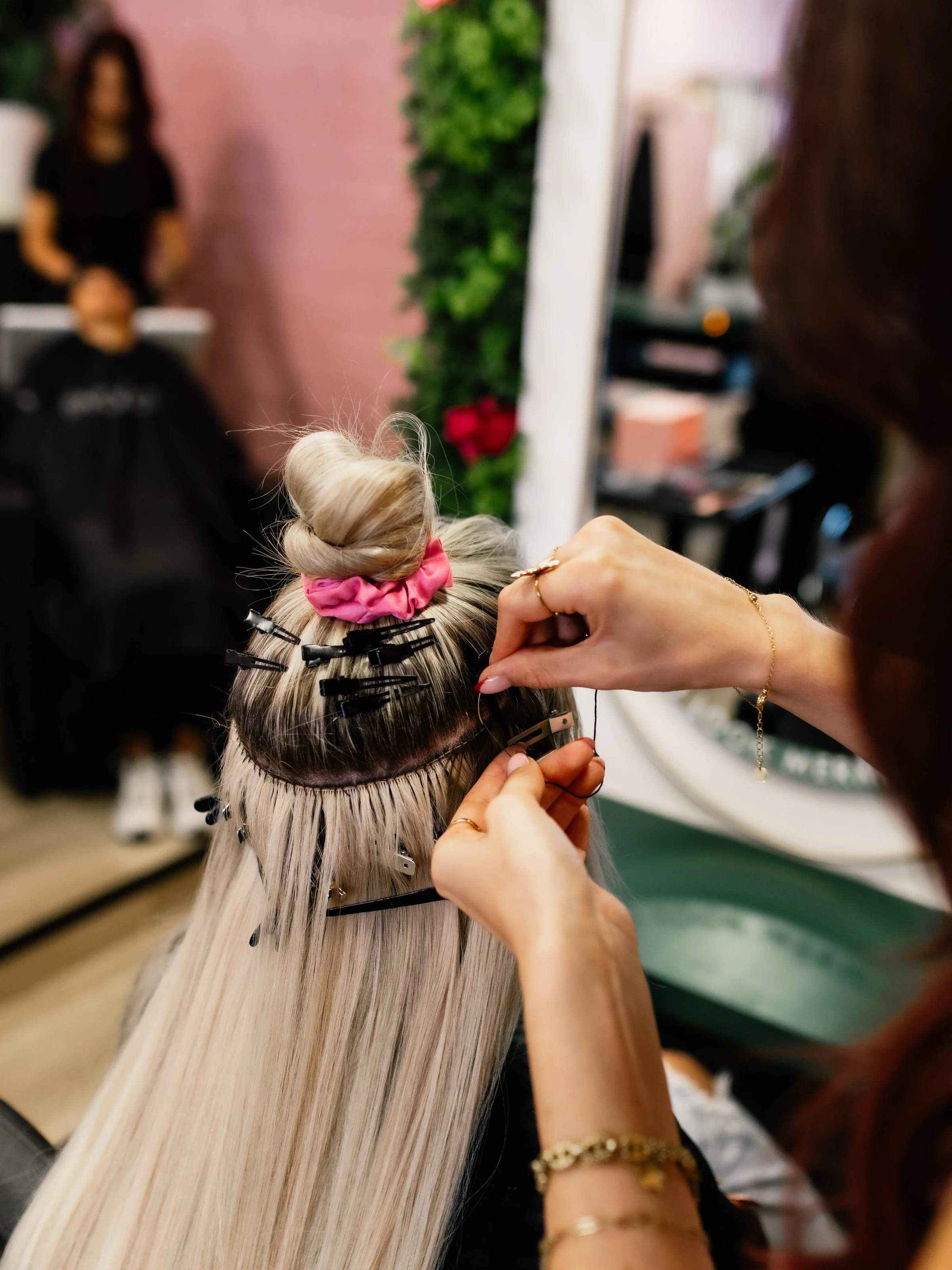 Stylist zet extensions bij een klant met een roze scrunchie in de knot