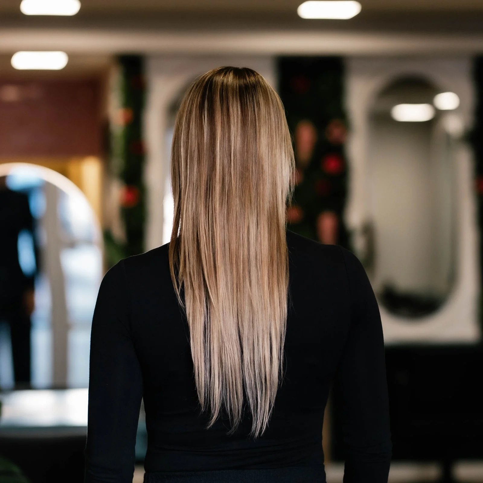 Klant met steil, lichtblond haar tot halverwege de rug, van achteren gezien, voor het zetten van extensions