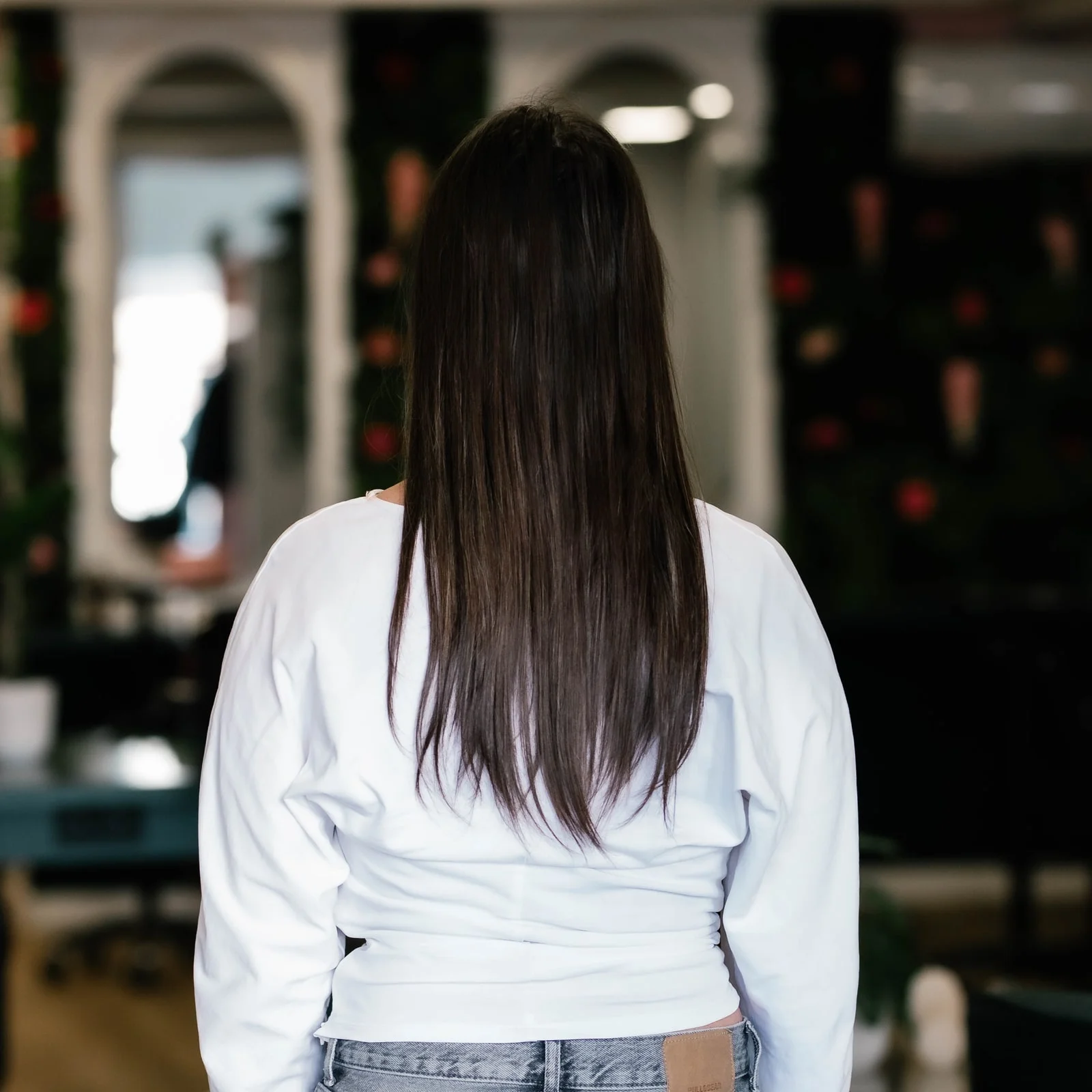 Klant met steil, lang donker haar van achteren, voor het zetten van extensions